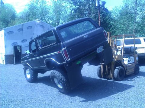 1979 Ford Bronco - A black 1979 Ford Bronco is being lifted by a yellow forklift, with another vehicle visible in the background.