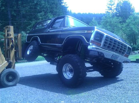 1979 Ford Bronco - A black Ford Bronco is lifted by a forklift, showing off its suspension and large tires.