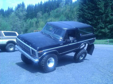 1979 Ford Bronco - Two Ford Broncos are parked outside. One is black and lifted, the other is tan.