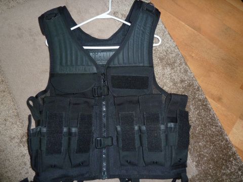 1992 Ford Mustang - A black tactical vest, possibly a Blackhawk brand, is displayed on a hanger against a carpeted floor and wooden planks.