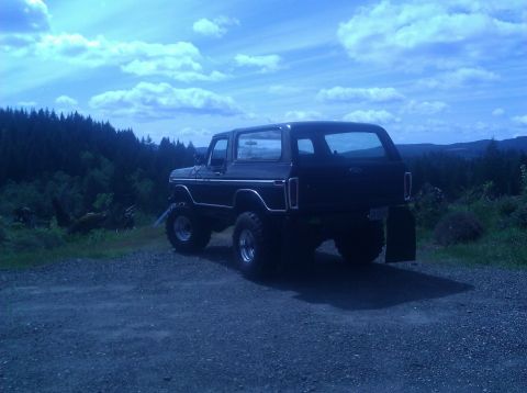 1979 Ford Bronco - This lifted Ford Bronco sits on a gravel lot, with a forest and cloudy sky behind it.