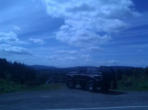 1979 Ford Bronco - A black 1978 Ford Bronco is parked on a gravel surface with a scenic mountain landscape in the background under a cloudy blue sky.
