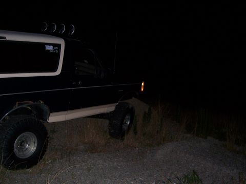 1992 Ford Bronco - A 1992 Ford Bronco is parked on a gravelly incline at night, with its headlights on.