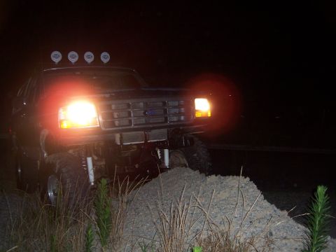 1992 Ford Bronco - This 1992 Ford Bronco is captured at night, equipped with four auxiliary lights on its roof, navigating an off-road terrain.
