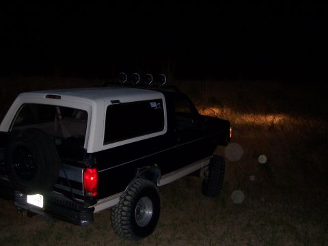 1992 Ford Bronco - A black and white Ford Bronco with a lifted suspension and roof lights is parked at night.