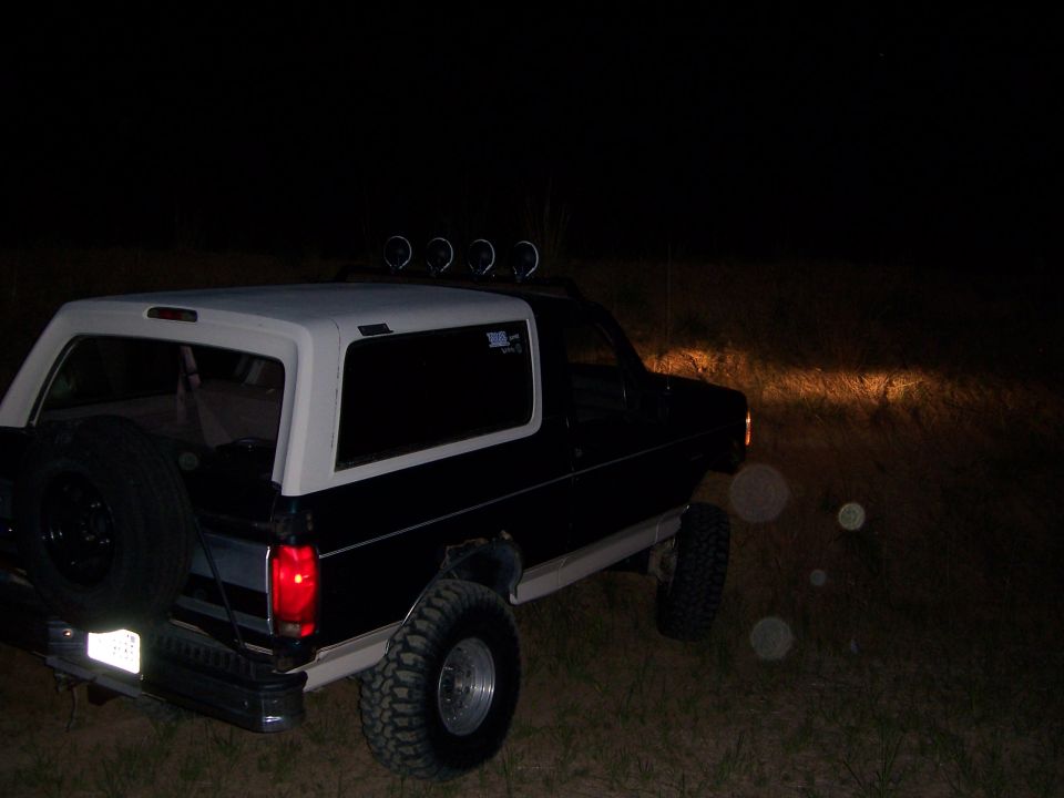 Black and white Ford Bronco with spare tire on back, lifted suspension, and roof lights