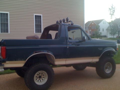 1992 Ford Bronco - Side view of a lifted 1992 Ford Bronco with off-road lights mounted on the roof rack.