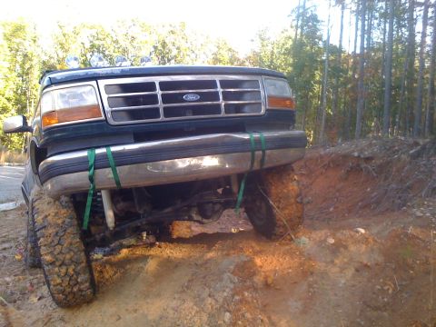 1992 Ford Bronco - A dark green Ford truck navigates a challenging off-road trail with large tires and a lifted suspension.