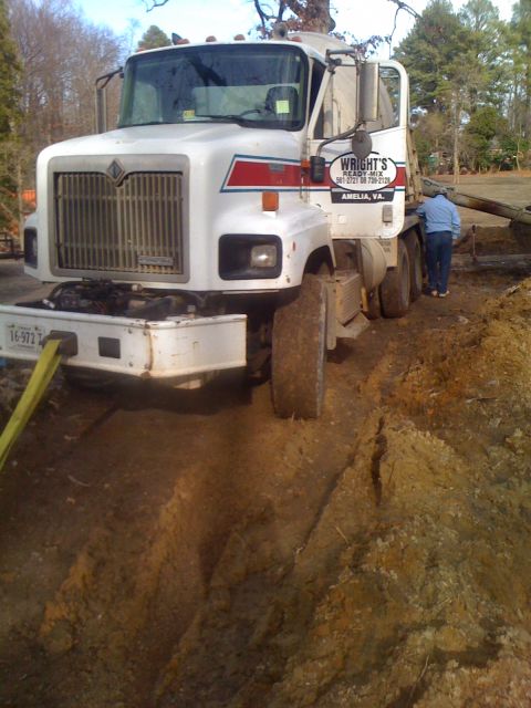 1992 Ford Bronco - A white cement truck is stuck in a muddy ditch, with a person standing near the driver's side door and a tow strap attached to the front.