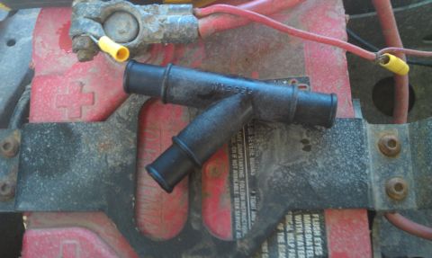 1978 Ford Bronco - Close-up of a black plastic Y-connector hose resting on a red car battery.