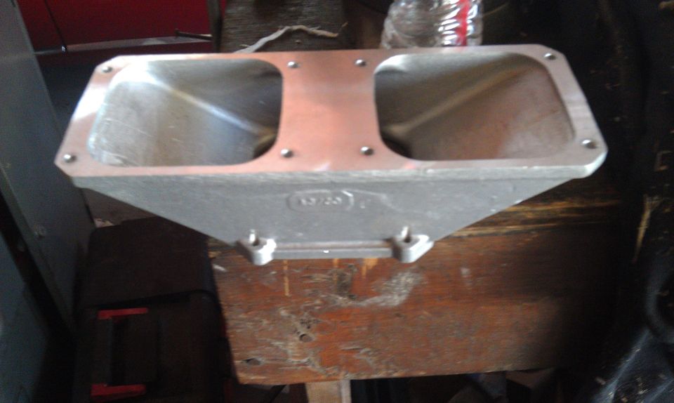 Aluminum intake manifold with two openings, resting on a wooden surface