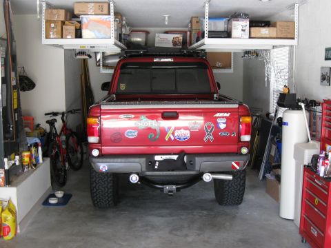 1999 Ford Ranger - Rear view of a red 1999 Ford Ranger pickup truck with custom wheels and stickers in a garage.