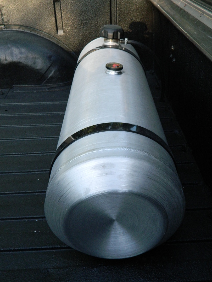 Cylindrical aluminum auxiliary fuel tank with black cap and gauge strapped in a black-lined truck bed