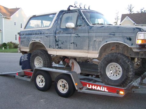 1992 Ford Bronco - A Ford Bronco is being loaded onto a U-Haul trailer, with two people attending to it from below.