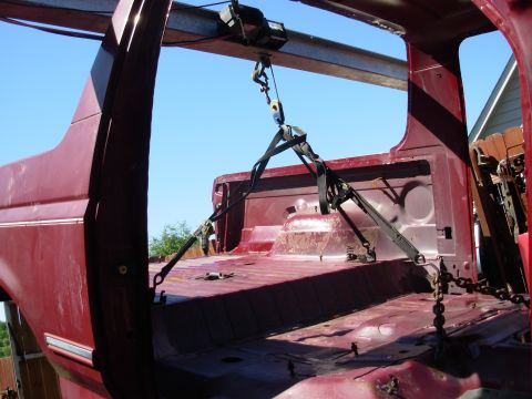 1983 Ford Bronco - The body of a red 1983 Ford Bronco is suspended by a crane, viewed from the rear.