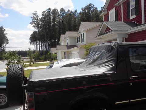 1992 Ford Bronco - A black 1992 Ford Bronco is parked in front of houses, with another white vehicle partially visible.