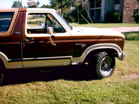 1980 Ford Bronco - A brown and white 1980 Ford Bronco is parked on a grassy lawn, with a building in the background.