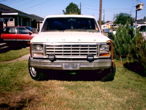 1980 Ford Bronco - Frontal view of a white 1980 Ford Bronco parked on a grassy lawn, with a red sedan visible in the background.
