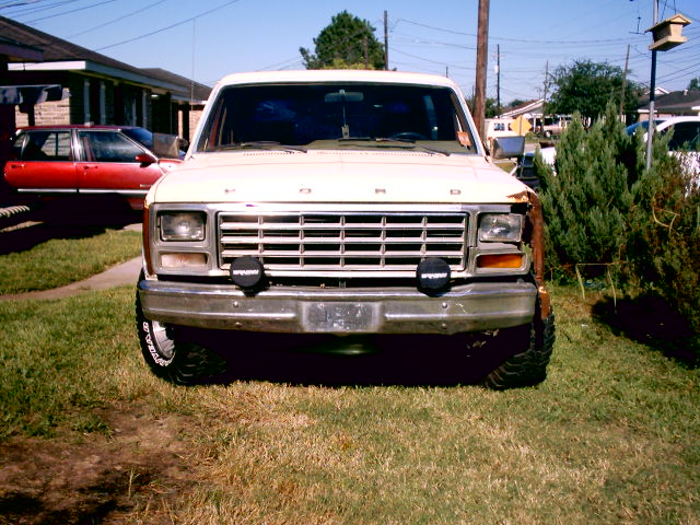 Front view of a white 1980 Ford Bronco with a red car in the background