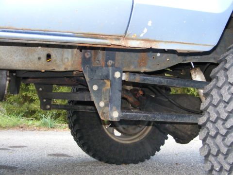 1978 Ford Bronco - The undercarriage of a light blue vehicle displays significant rust on its frame and body panels, with a large off-road tire visible.