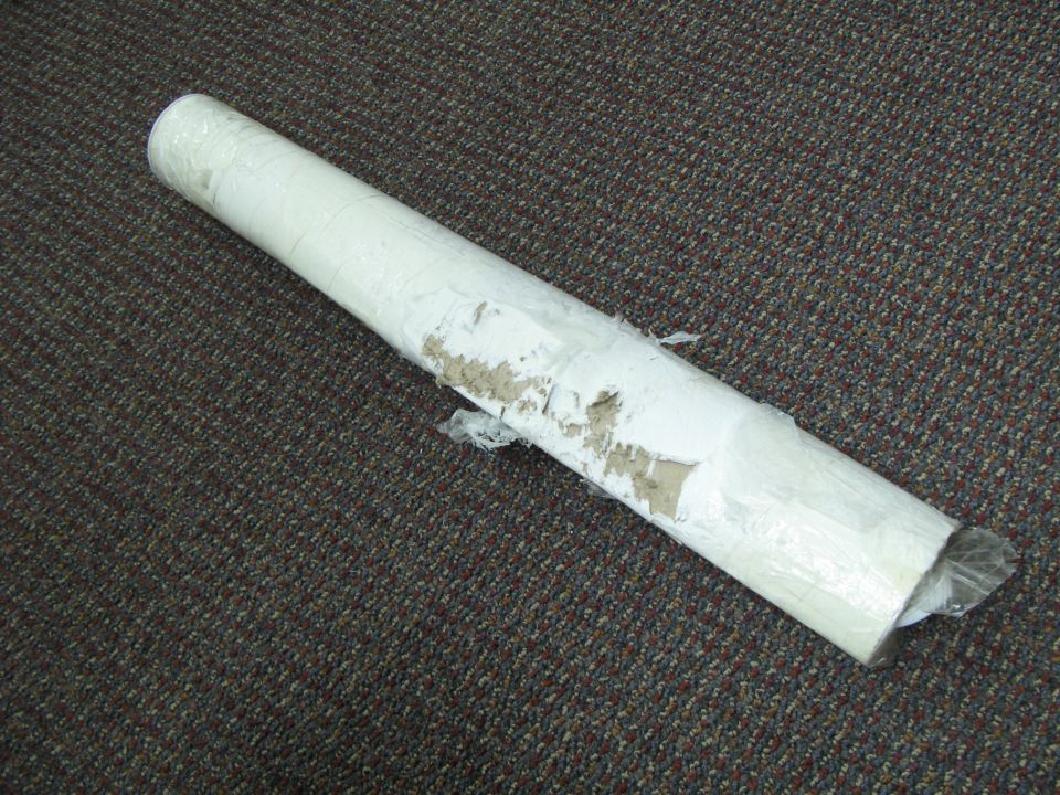 Rolled up item wrapped in white paper and plastic, on a carpeted floor. Supermotors.net logo in corner