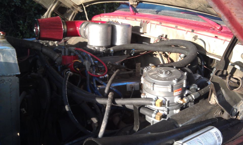 engine bay with red air filter, dual carburetors, and a propane conversion tank