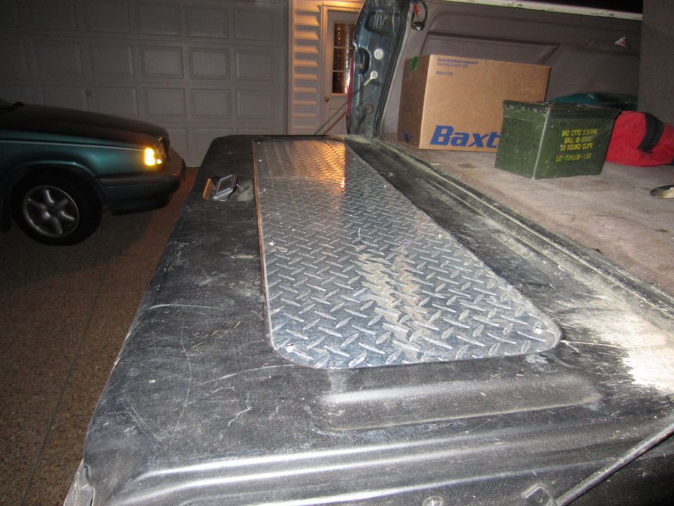 Truck bed with diamond plate cover, green sedan in background