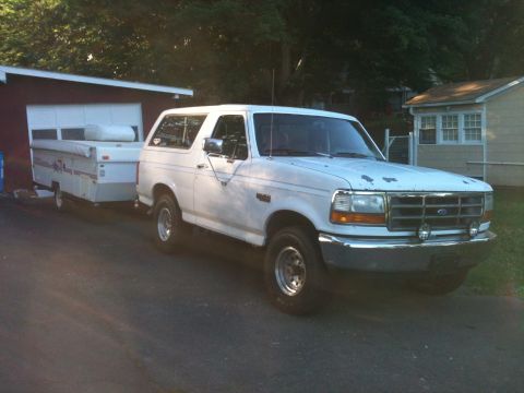 1992 Ford Bronco - A white 1992 Ford Bronco is parked next to a garage, hitched to a pop-up camper.