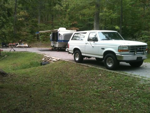 1992 Ford Bronco - A white 1992 Ford Bronco is parked at a campsite, hitched to a pop-up camper.