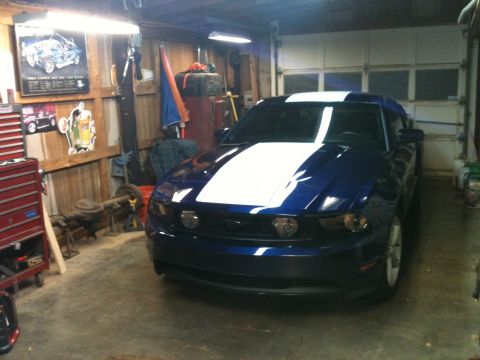 2010 Ford Mustang - Front view of a blue 2010 Ford Mustang with white racing stripes in a garage.