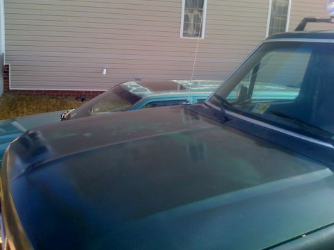 1992 Ford Bronco - Close-up view of a green SUV's hood and windshield, with another vehicle partially visible behind it.