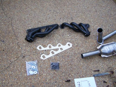 1992 Ford Bronco - Exhaust manifolds, catalytic converter, gaskets, and hardware are laid out on a concrete surface.