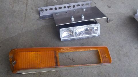 1978 Ford Bronco - Two vehicle lighting components, a headlight and an amber marker light, are laid out on a concrete surface.