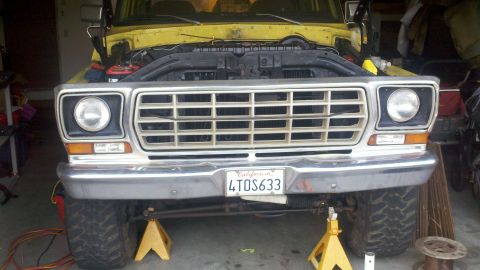 1978 Ford Bronco - Front view of a yellow 1978 Ford Bronco, hood open, on jack stands, showing the grille and bumper.