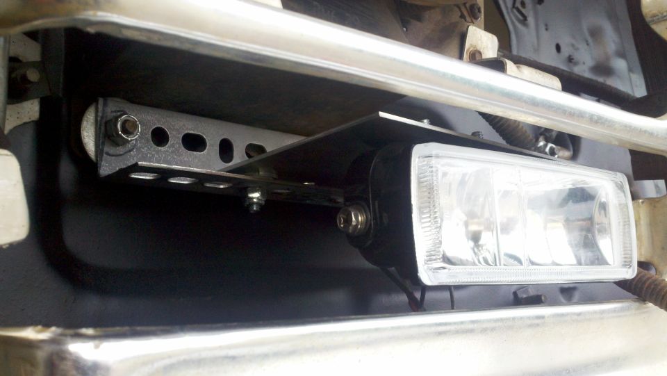 Aftermarket fog light mounted with a metal bracket below a chrome bumper