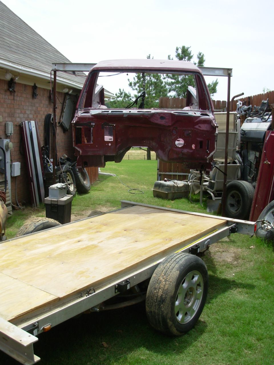 Burgundy Bronco cab shell hoisted in air above a flatbed trailer in a backyard