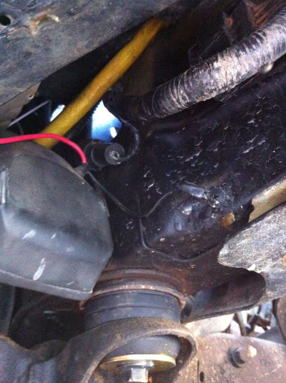 close-up of vehicle suspension parts, yellow wire, and wiring harness