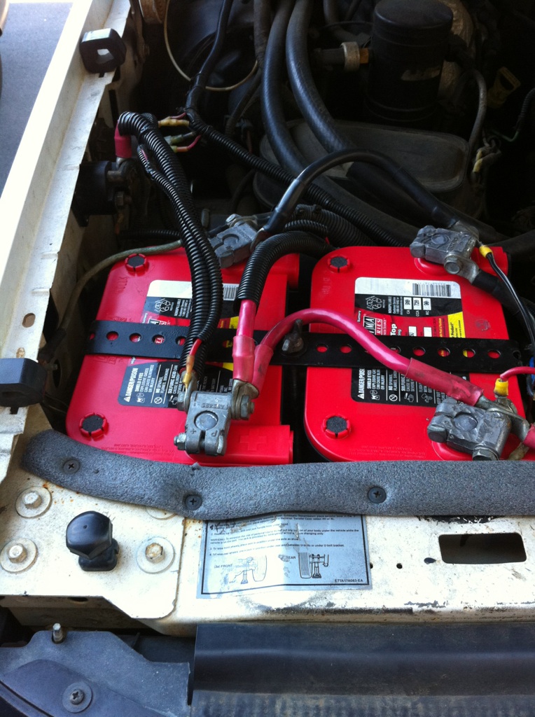 Dual red Optima batteries secured with black brackets in a vehicle engine bay