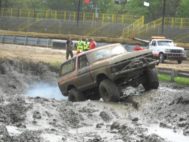1978 Ford Bronco navigating a muddy obstacle course, with a tow truck in the background