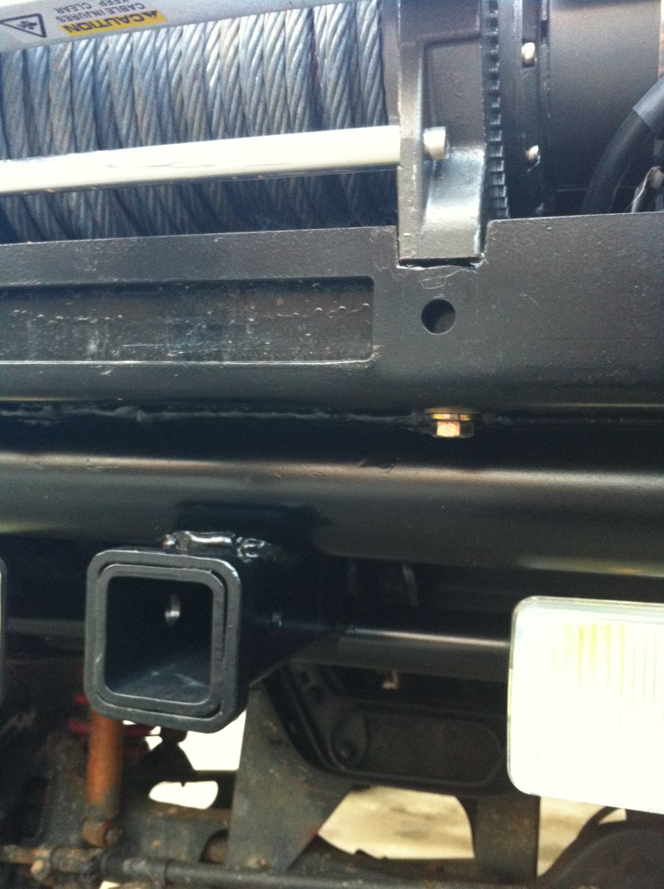Winch and trailer hitch receiver on black metal frame. Visible text: CAUTION KEEP CLEAR