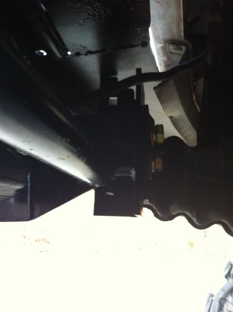 1996 Ford Bronco - Underbody shot looking up at a black-painted frame rail and rear leaf spring assembly, with a stack of spring leaves clamped at a shackle b…