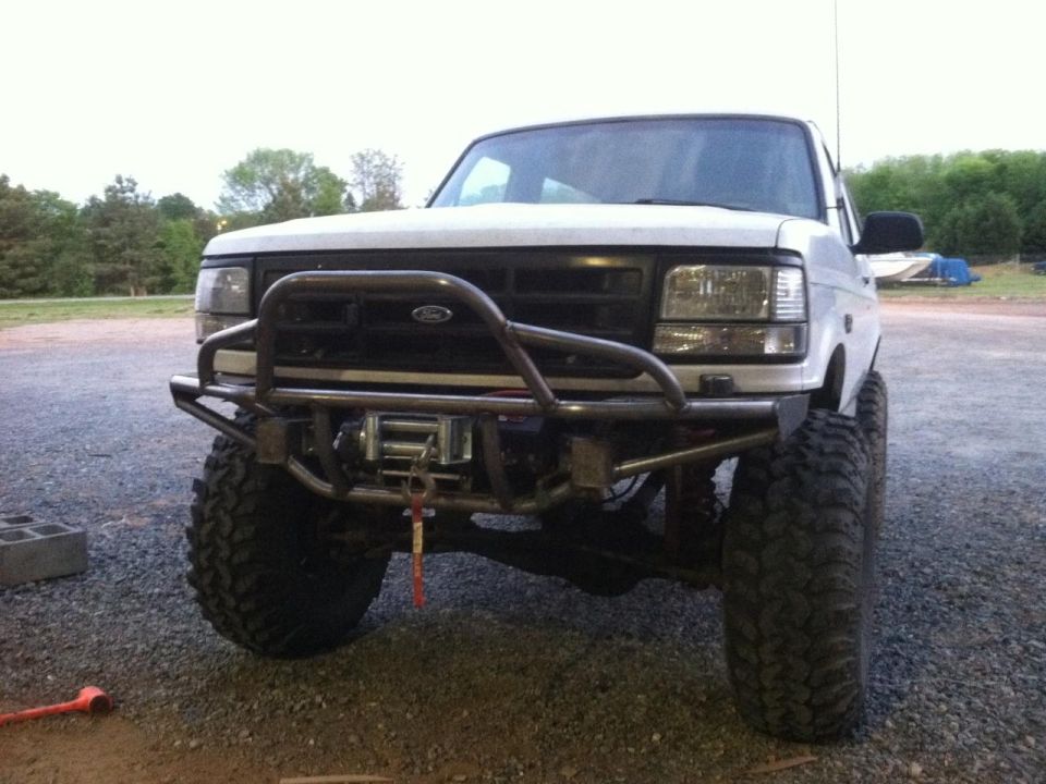 Lifted white Ford Bronco with steel tube bumper, winch and mud tires on gravel lot