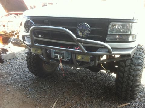 1996 Ford Bronco - Custom bumper and winch assembly on a white Ford Bronco, aftermarket PIAA lights and aggressive off-road tires.