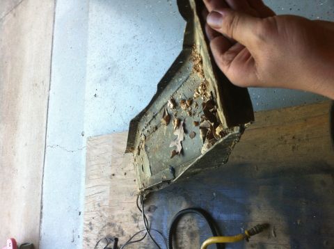 1996 Ford Bronco - A hand holds up a removed stamped-steel body panel or battery tray, its inside face crusted with dirt, dry leaves and debris and rusting al…