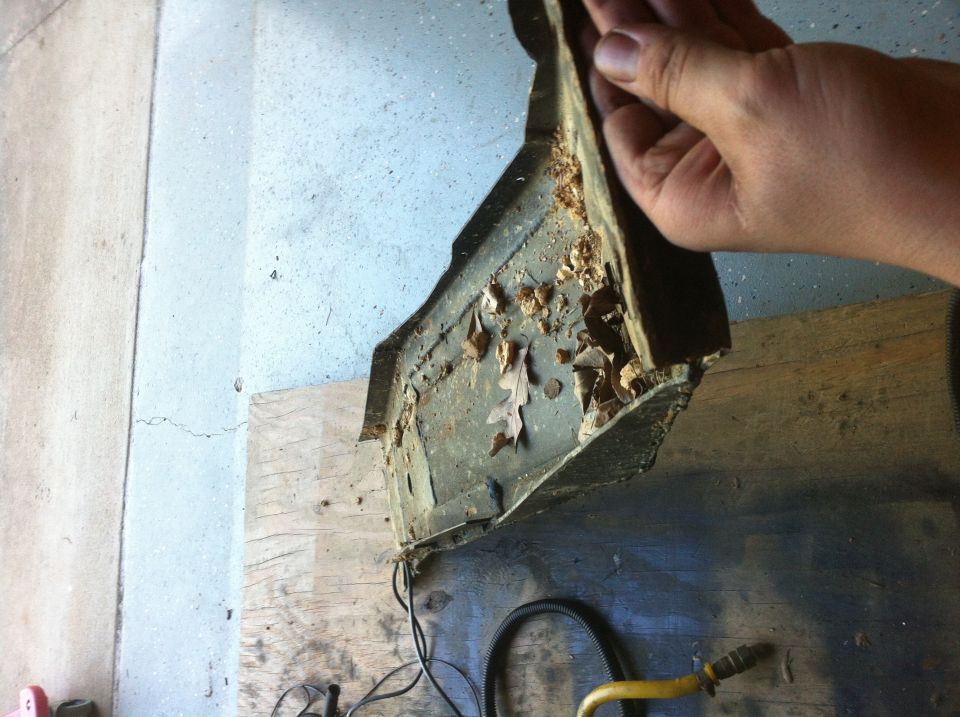 Hand holding a rusty leaf-filled stamped steel panel removed from a vehicle over a workbench