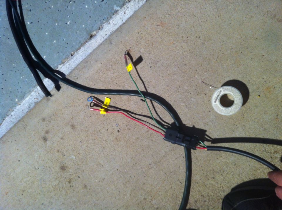 Automotive wiring harness with black and red wires connected to a black connector, with a roll of solder nearby