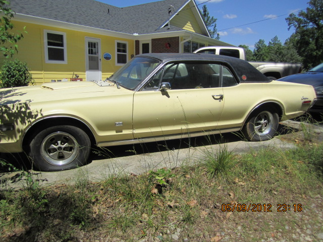 Yellow Mercury Cougar with black vinyl top parked outside a yellow house