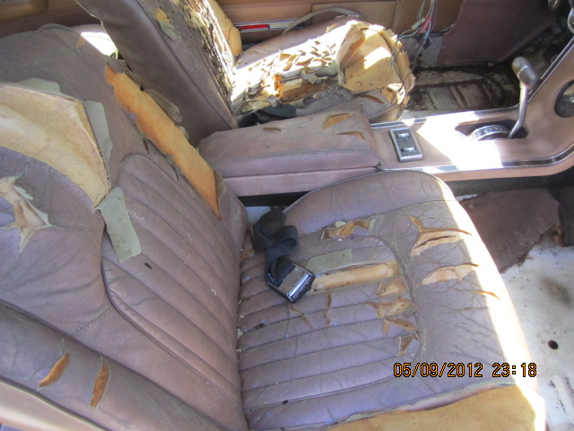 Car interior with torn seats and exposed foam. Seatbelt buckle visible