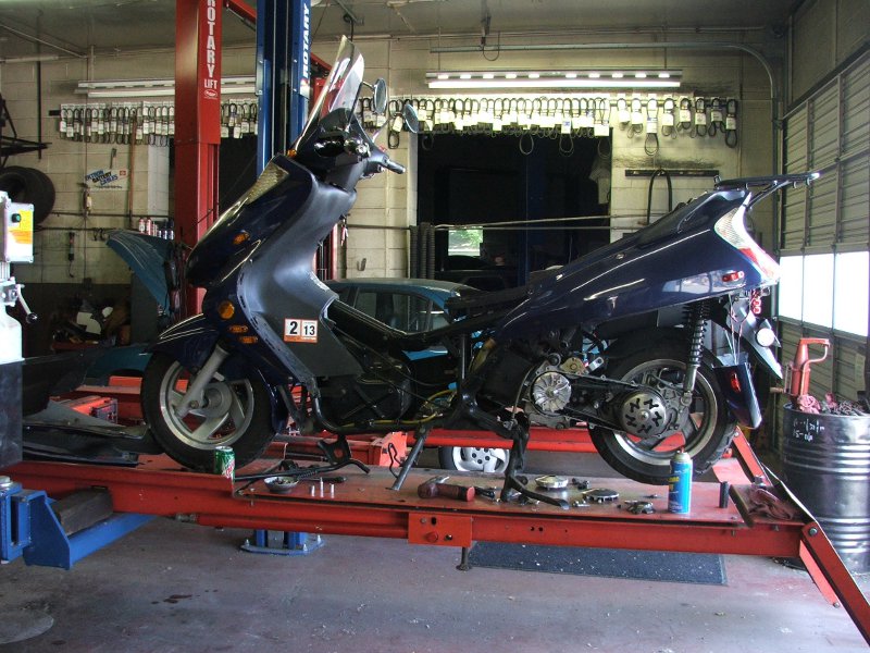 Dark blue scooter on a lift in a garage, with tools scattered on the lift platform