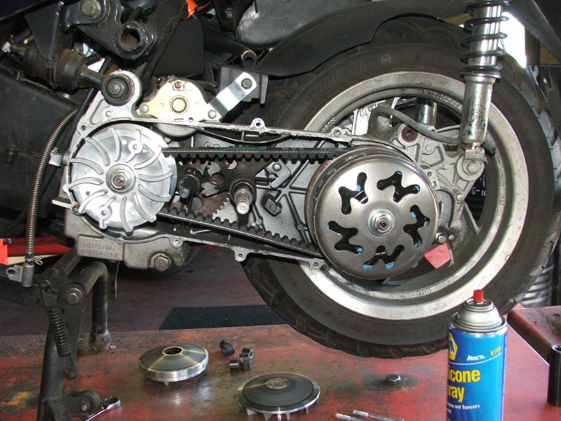 Scooter's drive belt and clutch assembly are exposed, with parts laid out on a workbench